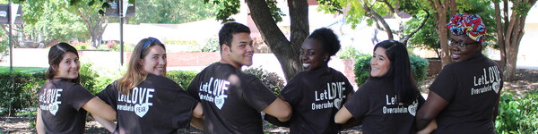 Students locked arms looking over their shoulder with matching t-shirts that say on the back Let Love Overwhelm Fear.