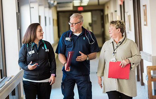 Three nursing administrators walk and talk in a hospital hallway.