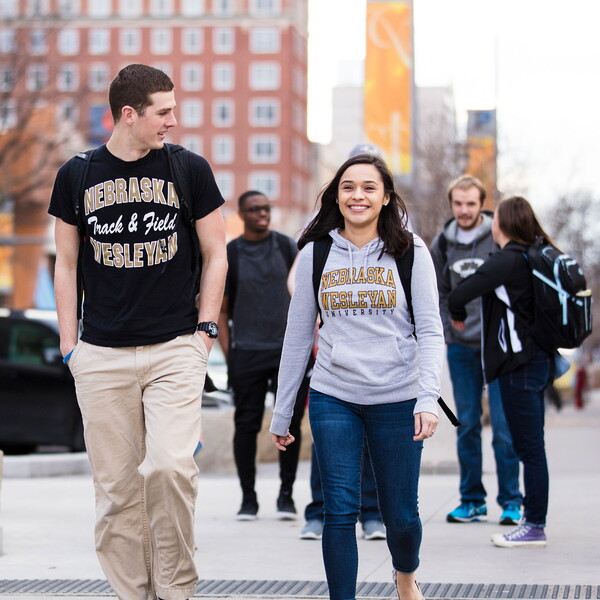 Two students walk in front of another group of students in downtown Lincoln.