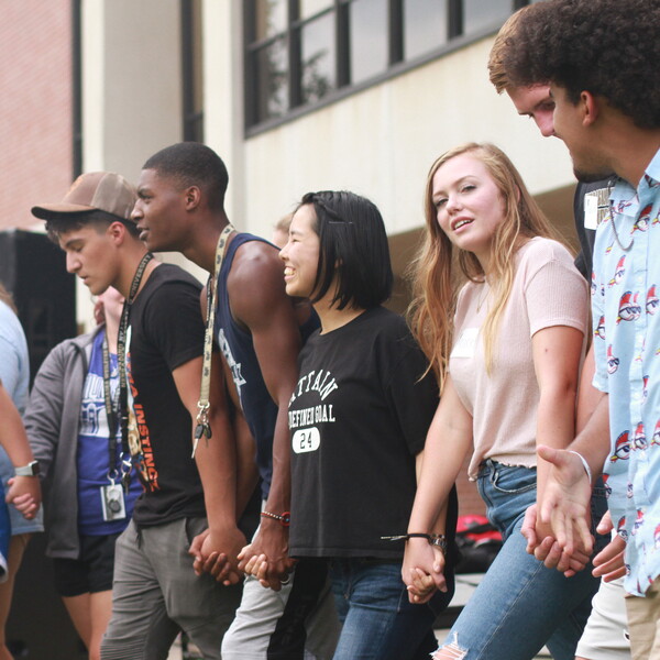 A group of students holding hands and smiling broadly.