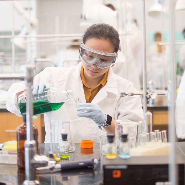 Female chemistry student pouring green liquid into small beaker