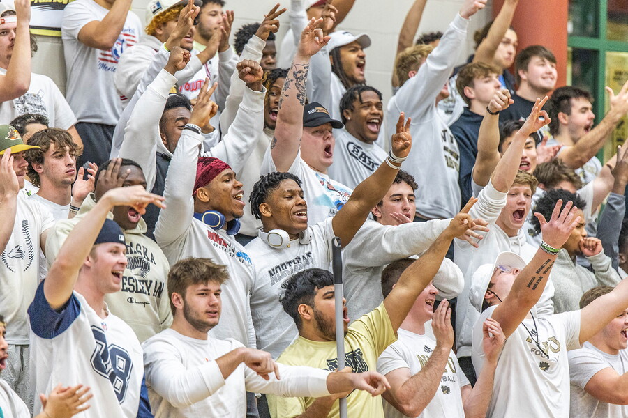 Basketball stands full of students with hands in the air cheering.