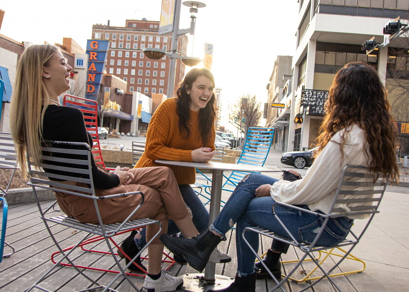 Four female NWU students sit at a table on the sidewalk of downtown Lincoln.