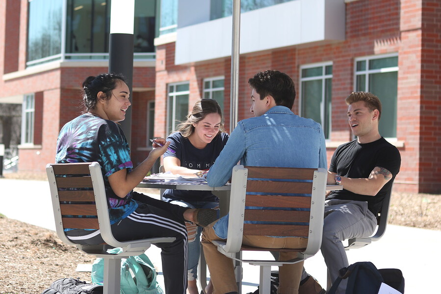 a group of four students sitting at an table outside laughing and talking