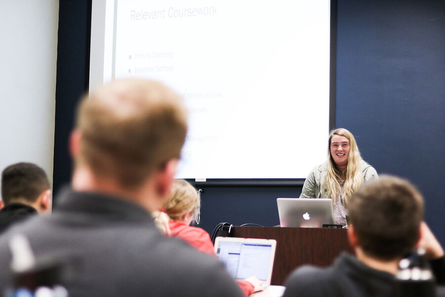 Young woman at a podium smiling in front of a class