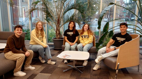 Five students sitting in a line on chairs and a couch.