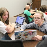 Students at a table looking at computers.